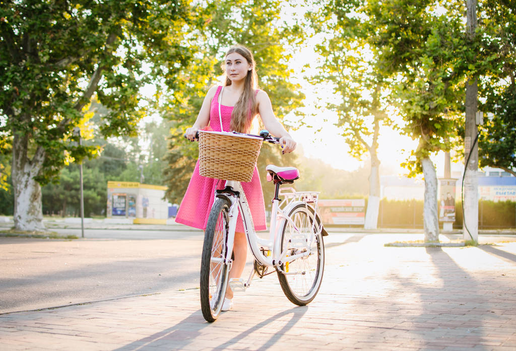 Jeune femme avec vélo de ville allant dans le parc au lever ou au coucher du soleil
 - Photo, image