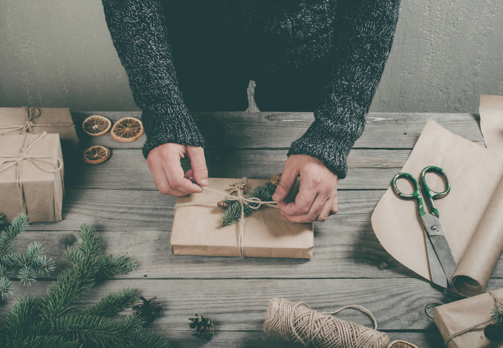 Мужские руки, заворачивающие рождественский подарок на деревянный стол
 - Фото, изображение