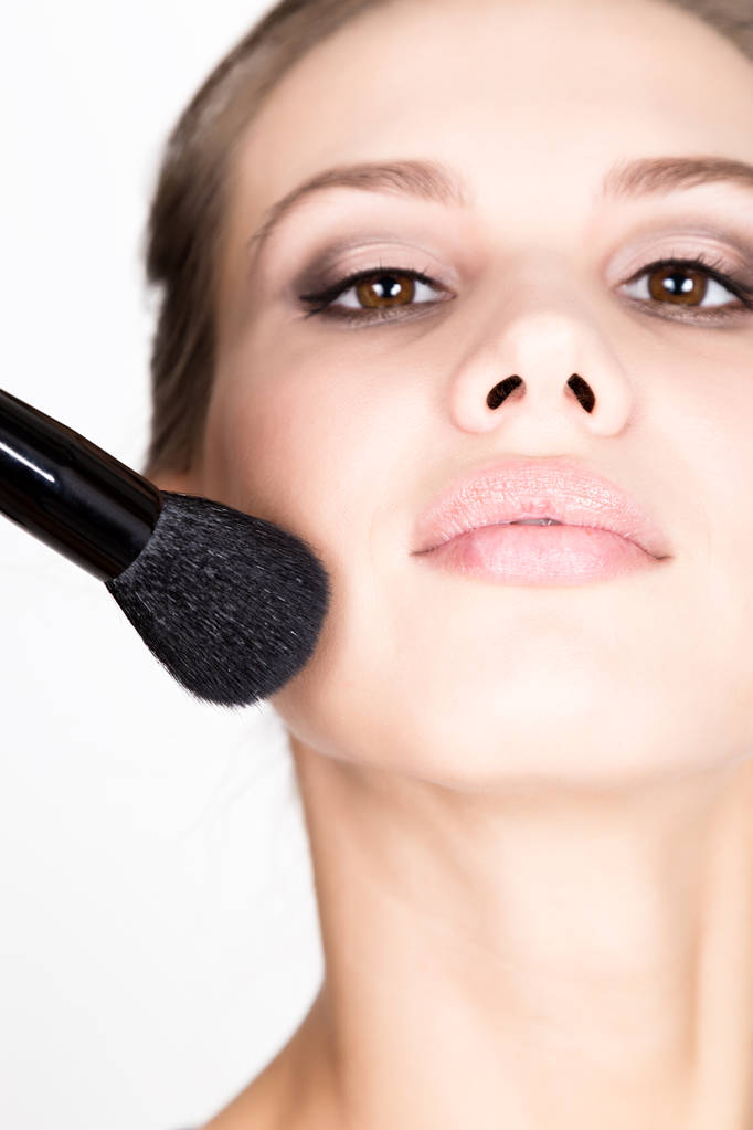 Close-up modelo feminino aplicando maquiagem em seu rosto. Mulher bonita aplicando fundação em seu rosto com uma escova de maquiagem
. - Foto, Imagem