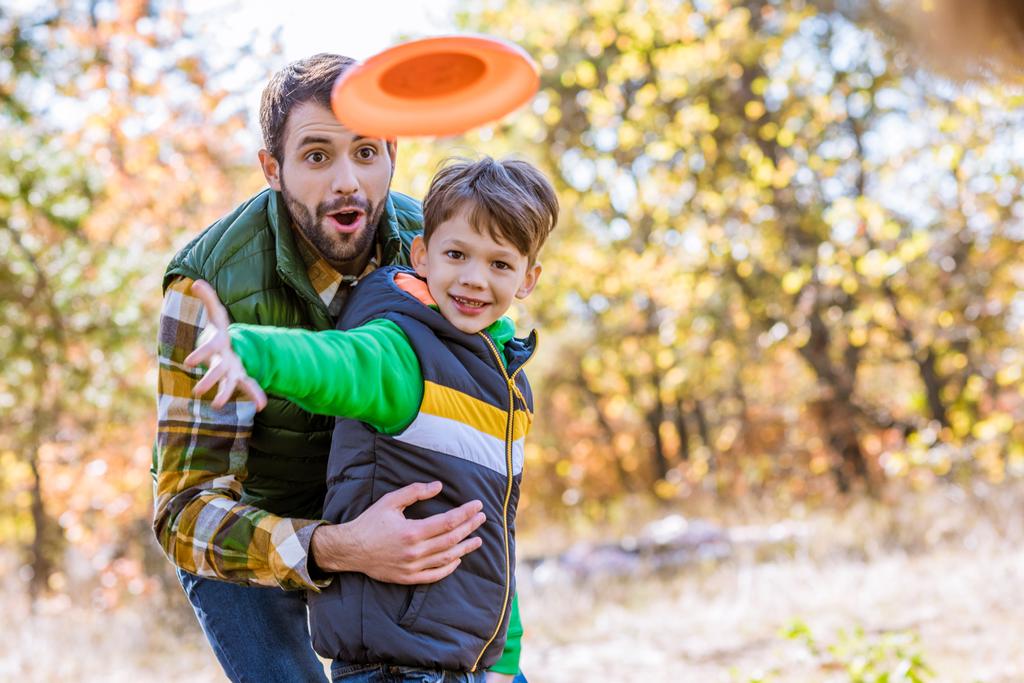 Lachende vader en zoon spelen met frisbee - Foto, afbeelding