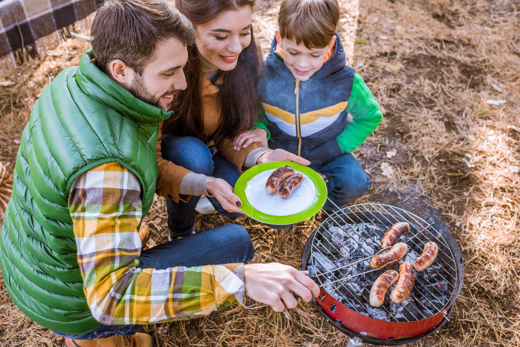 Cheerful parents with son grilling sausages - Photo, Image