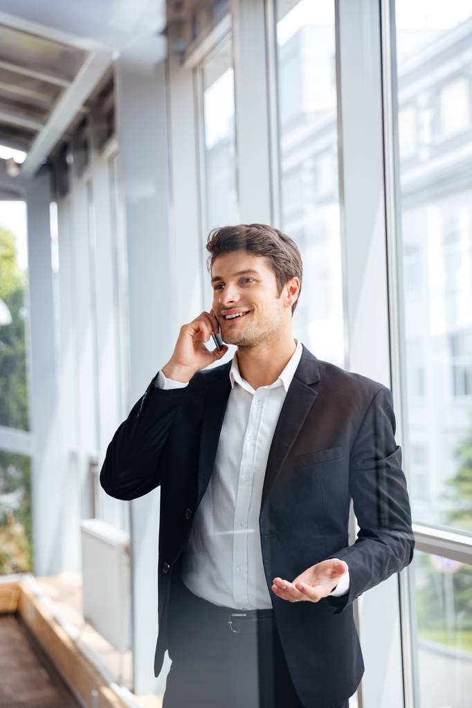 Vrolijke jonge zakenman praten op mobiele telefoon in kantoor - Foto, afbeelding