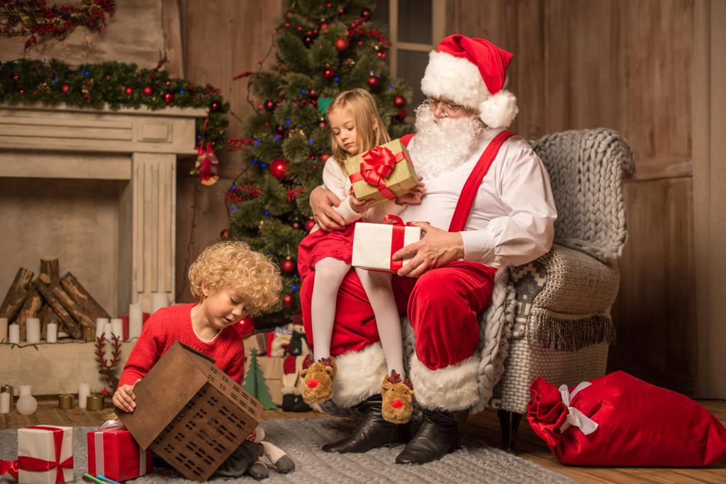 Kerstman met kinderen zitten in de buurt van open haard  - Foto, afbeelding