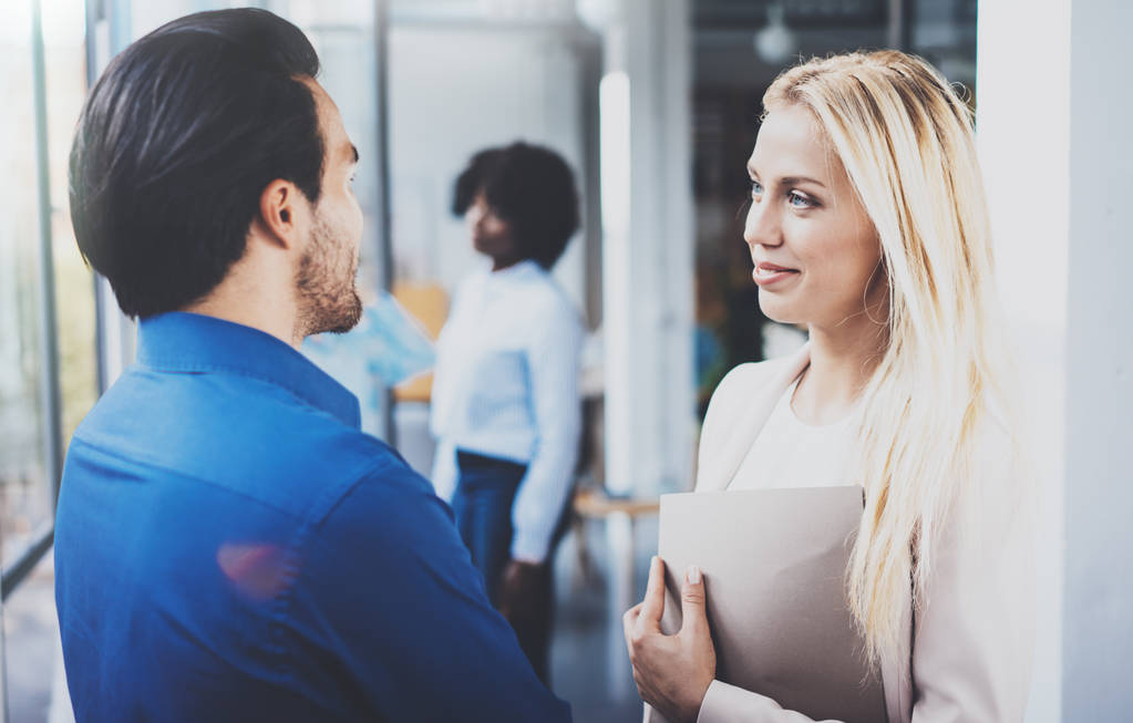 Two coworkers discussing business strategy in modern office.Successful confident hispanic businessman talking with blonde woman. Horizontal, blurred background. - Photo, Image