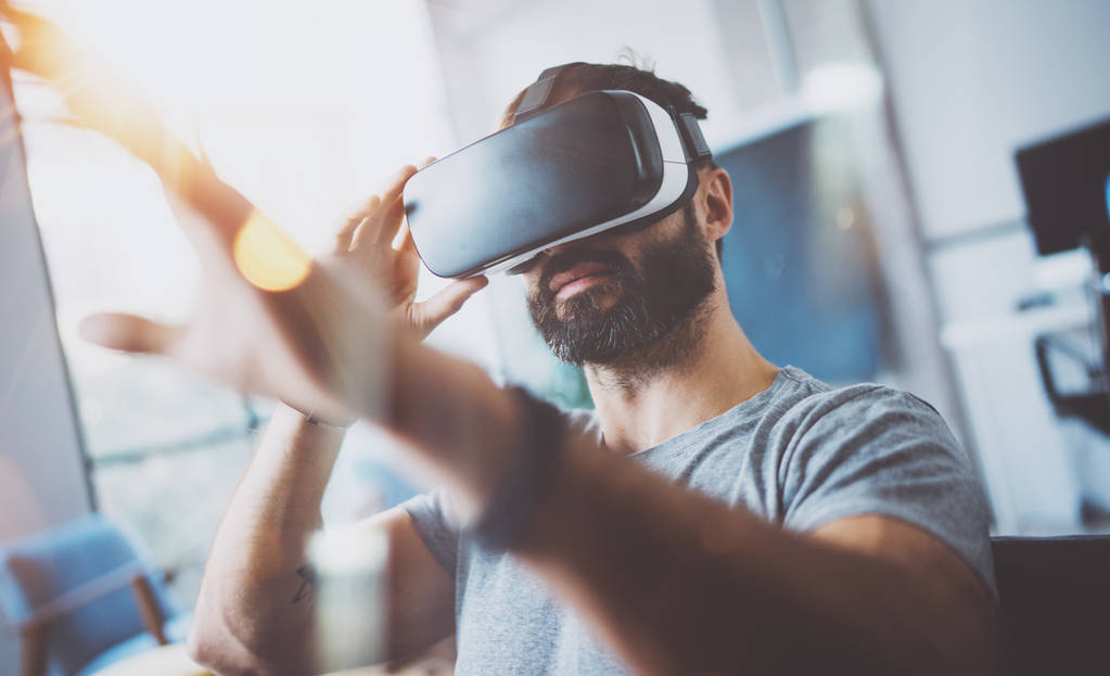Primer plano del joven barbudo con gafas de realidad virtual en el moderno estudio de coworking. Smartphone con auriculares VR. Horizontal, borrosa
. - Foto, Imagen