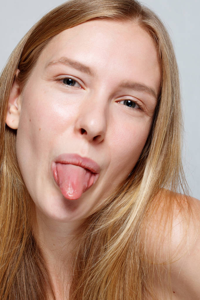 Młoda ładna kobieta strzela się języka, na szarym tle - Zdjęcie, obraz