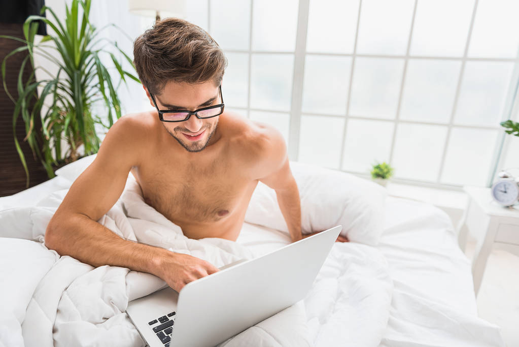 fröhlicher Kerl unterhält mit Computer im Schlafzimmer - Foto, Bild