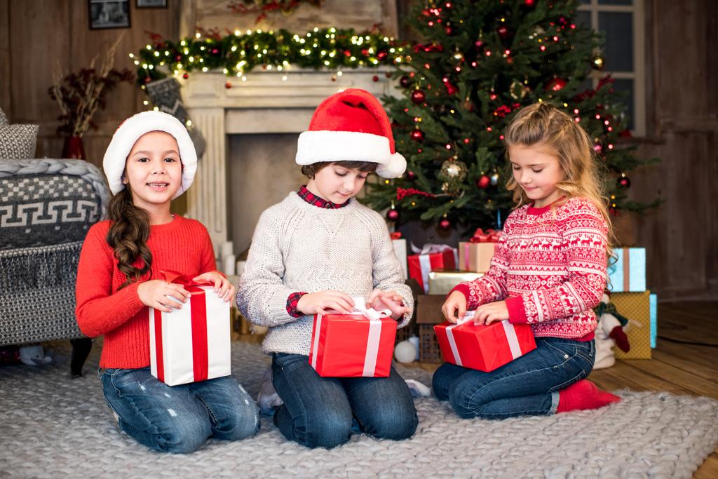 Дети в шляпах Санта-Клауса с подарочными коробками
 - Фото, изображение