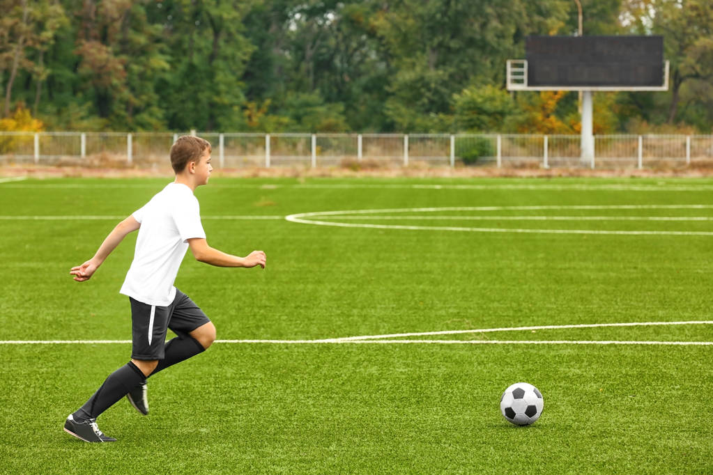 Мальчик играет в футбол на стадионе
 - Фото, изображение