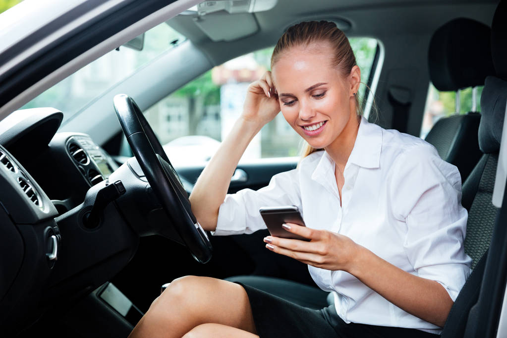 Hymyilevä liiketoiminnan nainen soittaa puhelinnumeroon istuessaan autossa
 - Valokuva, kuva