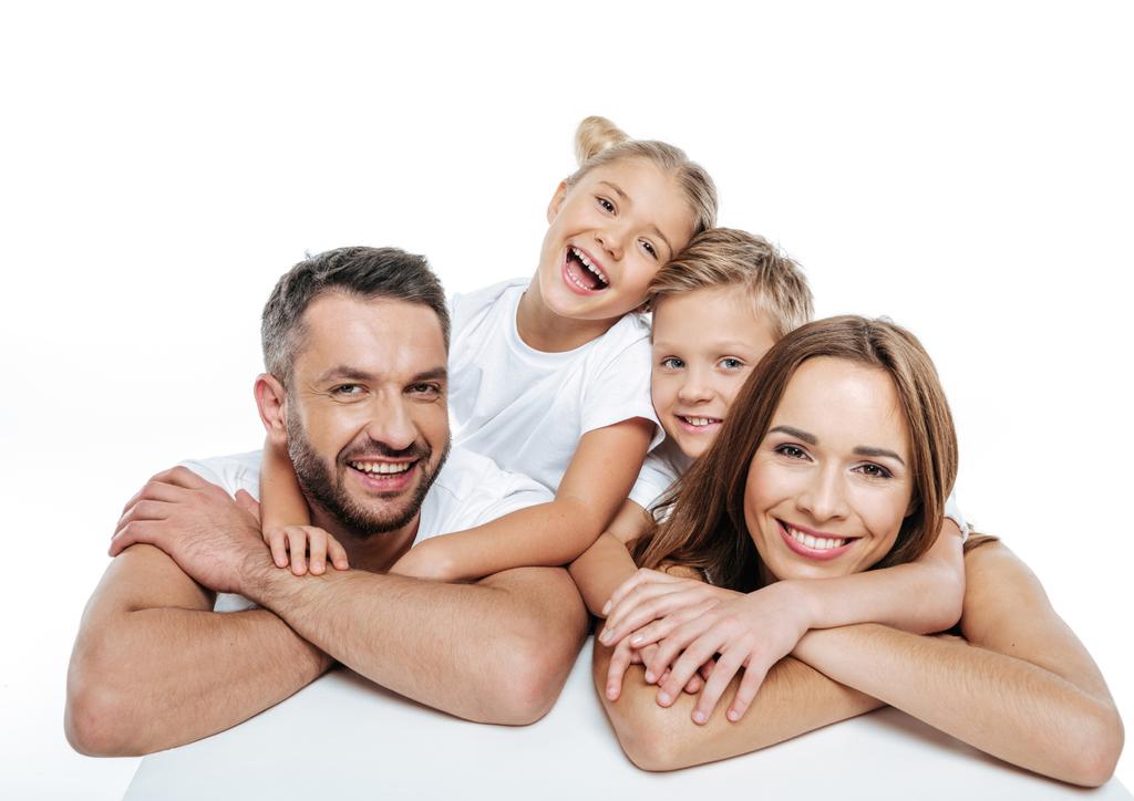Χαμογελώντας οικογένεια σε λευκά μπλουζάκια αγκάλιασμα  - Φωτογραφία, εικόνα