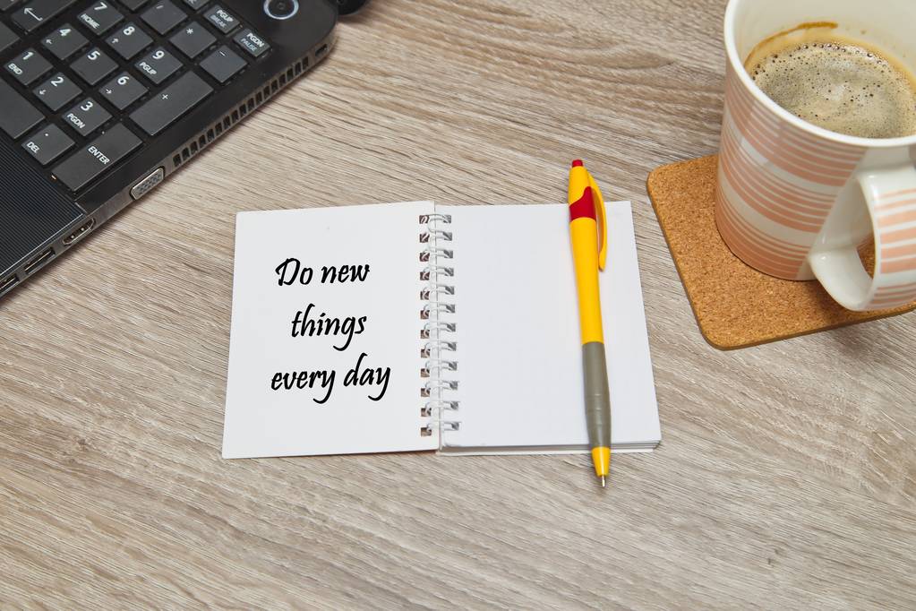 Abra el cuaderno con formas de "Hacer cosas nuevas todos los días" y una taza de café sobre fondo de madera. Vista de arriba hacia abajo
 - Foto, imagen