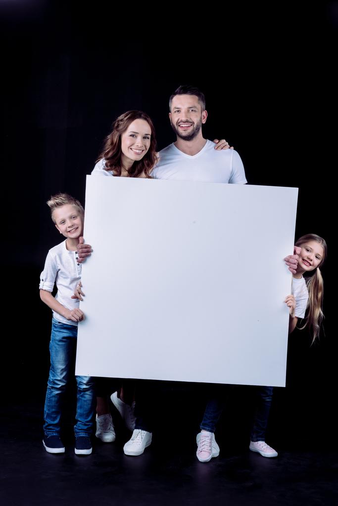 Familia sonriente sosteniendo tarjeta en blanco
 - Foto, Imagen