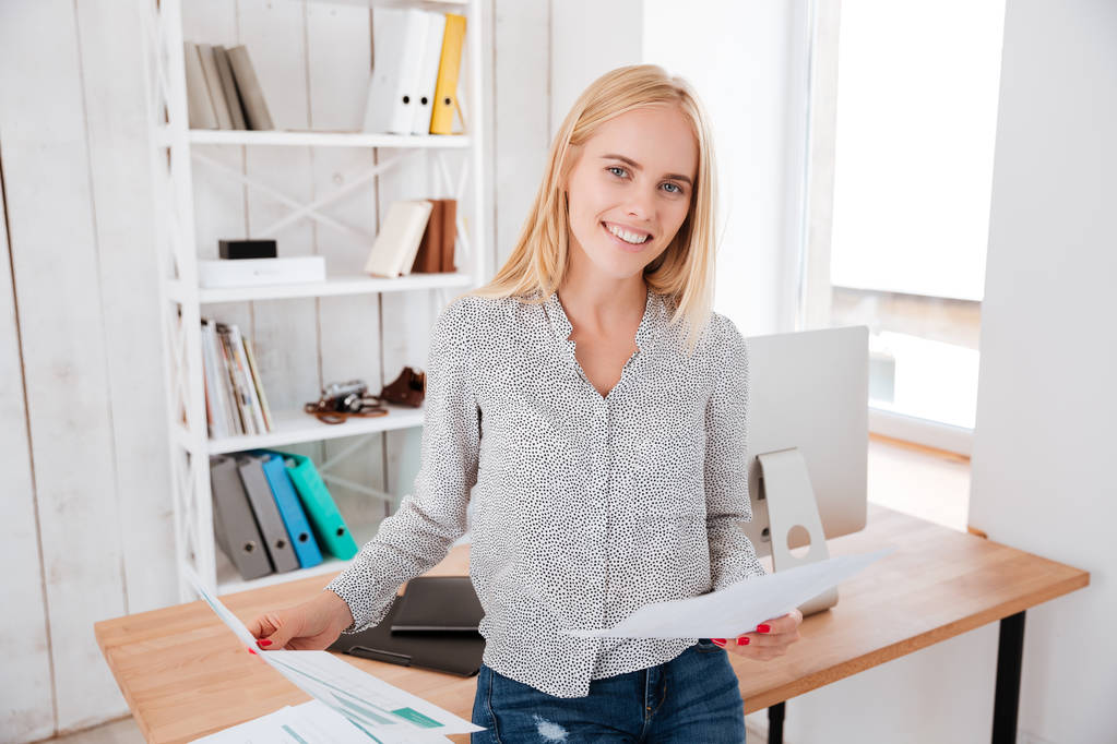 attraktive Geschäftsfrau, die Dokumente in der Hand hält und auf dem Bürotisch sitzt - Foto, Bild