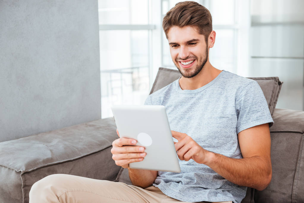 glücklicher Mann sitzt auf Sofa und plaudert per Tablet - Foto, Bild