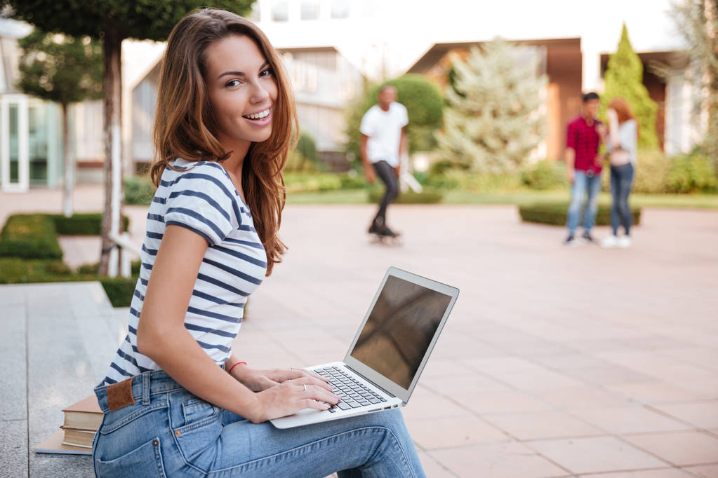 lächelnde süße junge Frau, die mit Laptop im Freien arbeitet - Foto, Bild