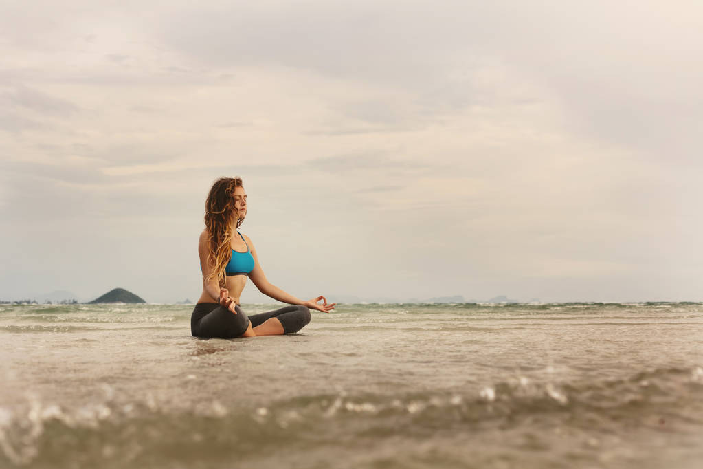 Женщина, сидящая на берегу моря и занимающаяся йогой
 - Фото, изображение