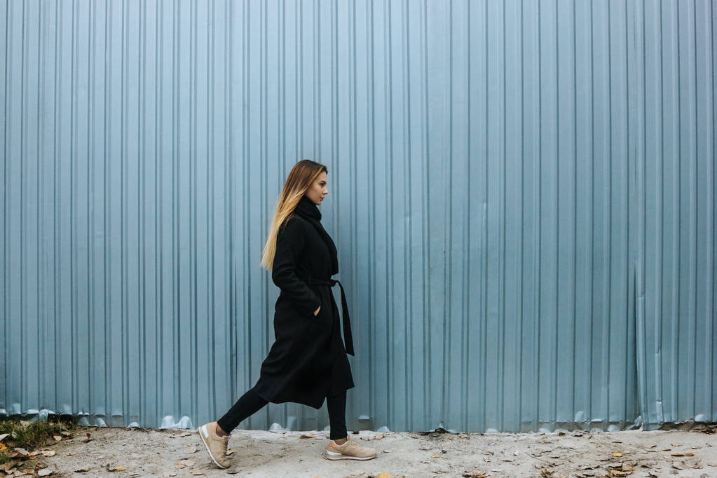 Όμορφη νεαρή γυναίκα με casual ρούχα περπάτημα ενάντια στο φράχτη - Φωτογραφία, εικόνα
