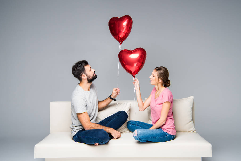 Pari istuu sohvalla punaisten ilmapallojen kanssa
 - Valokuva, kuva