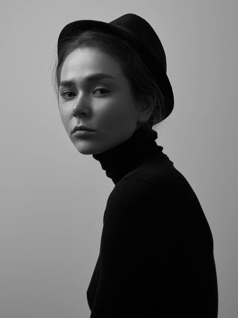 Δραματική ασπρόμαυρο πορτρέτο του όμορφη κοπέλα με φακίδες σε ένα μαύρο ζιβάγκο και ένα καπέλο σε λευκό φόντο στο studio - Φωτογραφία, εικόνα