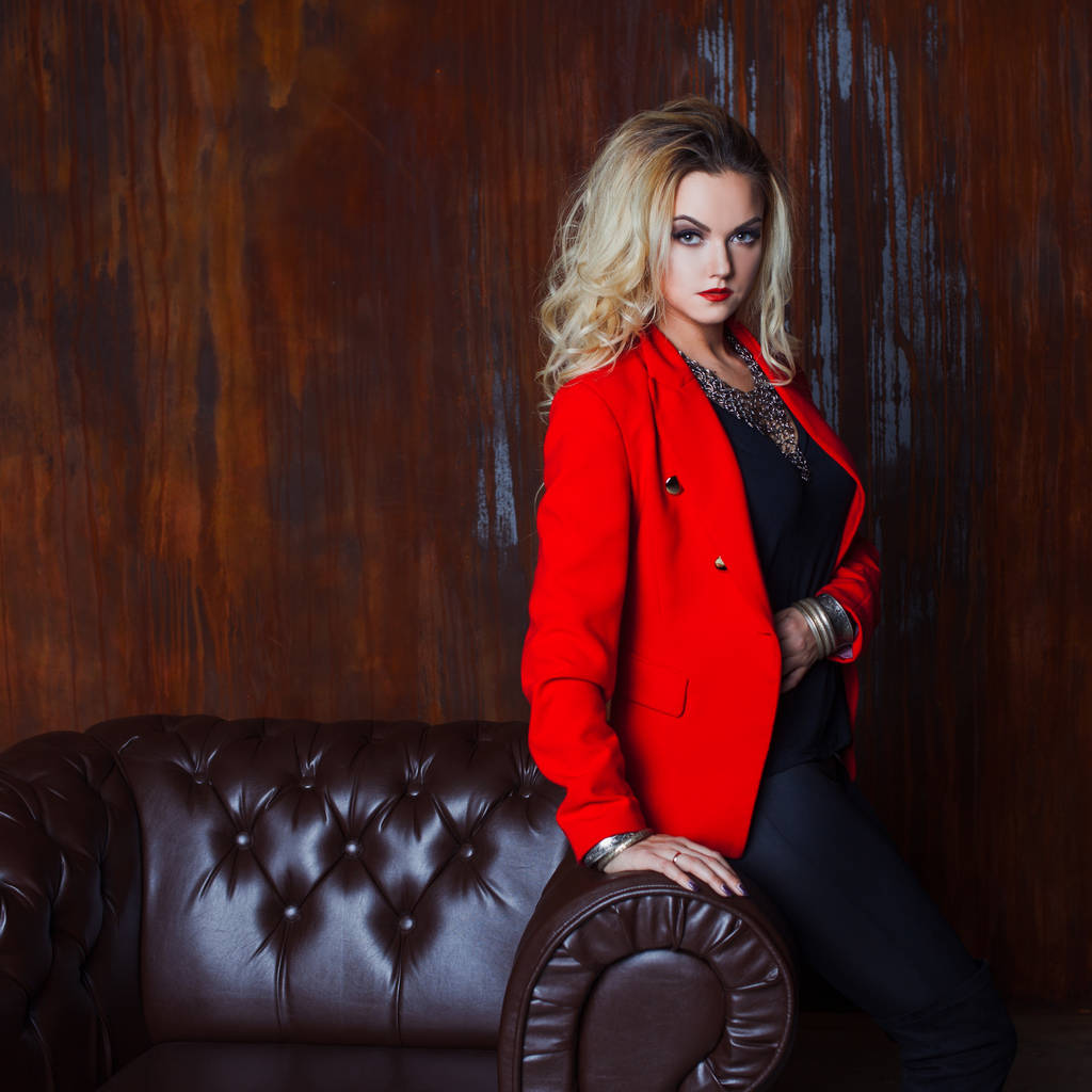 Молода і приваблива блондинка в червоній куртці, фон гранжева іржава стіна
 - Фото, зображення