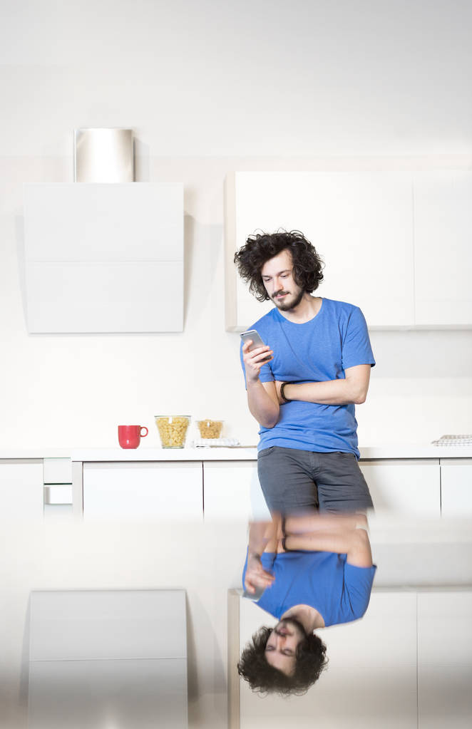 Чоловік на кухні за допомогою мобільного телефону
 - Фото, зображення