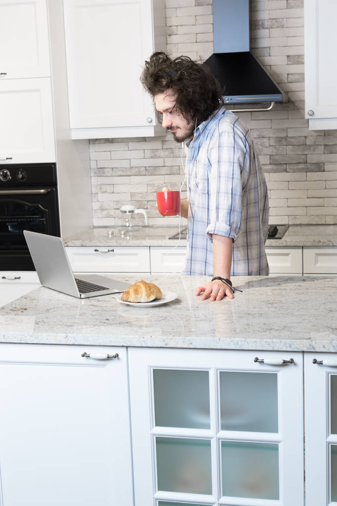 Mies syö aamiaista kannettavan tietokoneen käytön aikana
 - Valokuva, kuva