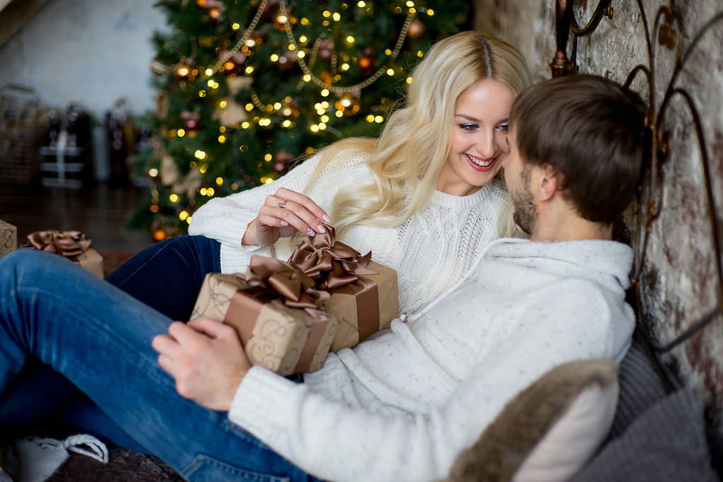Счастливая пара влюбленных в белых свитерах дарят друг другу подарки
 - Фото, изображение