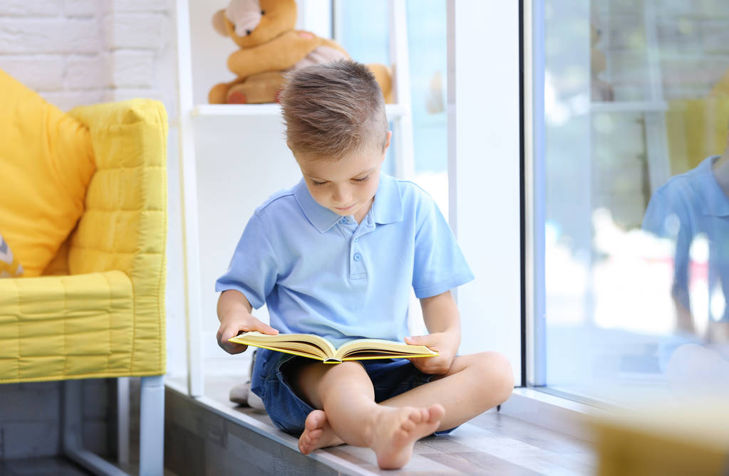 Симпатичный мальчик читает интересную книгу на подоконнике
 - Фото, изображение
