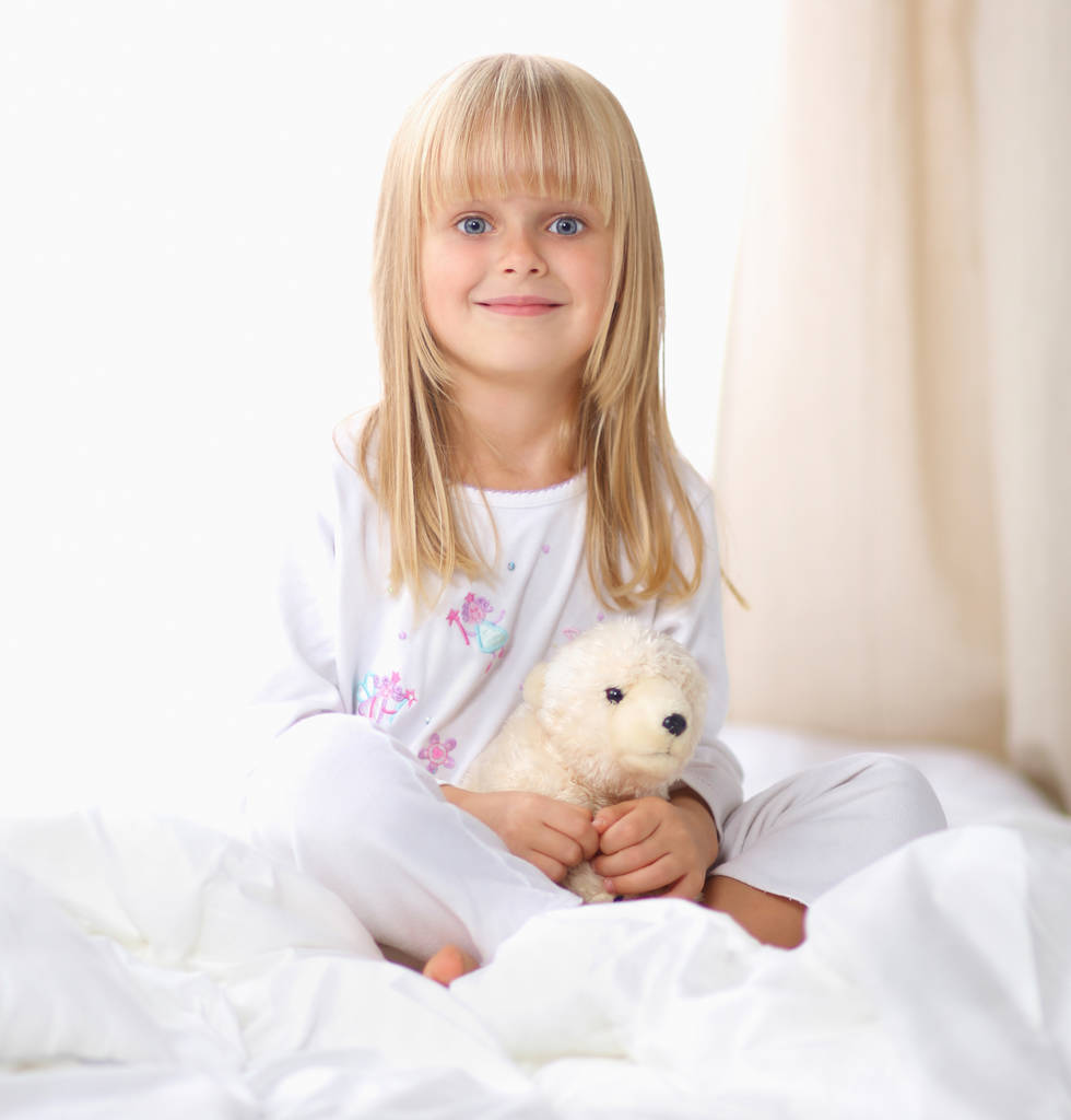 Meisje met teddy beer liggend op het bed thuis - Foto, afbeelding