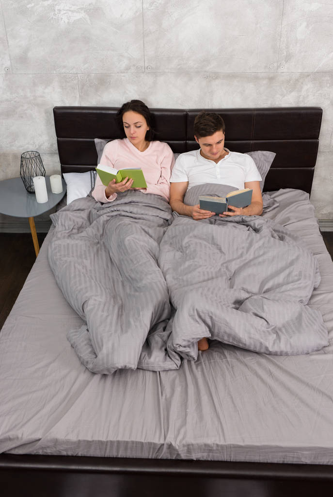 Giovane coppia concentrata leggere libri mentre sdraiato nel letto e
 - Foto, immagini