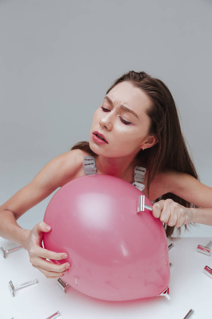 Mujer sosteniendo y aplicando hoja de afeitar vieja al globo rosa
 - Foto, Imagen