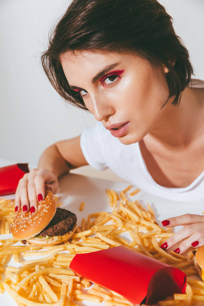 Donna seduta a tavola con hamburger e patatine fritte
 - Foto, immagini