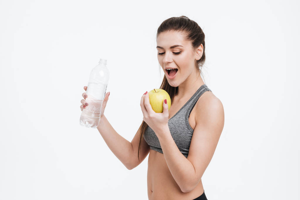 Молода спортивна жінка тримає пляшку води і кусає яблуко
 - Фото, зображення