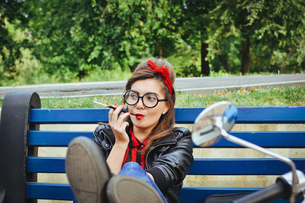 Giovane donna hipster in occhiali seduta su una panchina e fumare sigaretta
 - Foto, immagini
