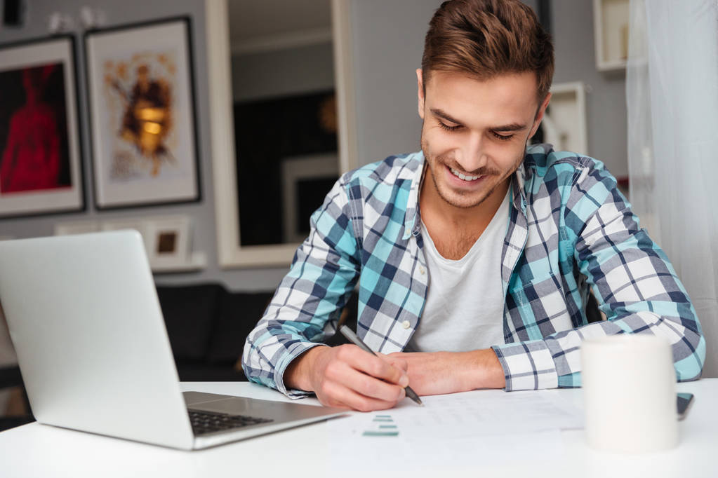 Hombre cerda alegre usando computadora portátil mientras analiza las finanzas del hogar
. - Foto, imagen