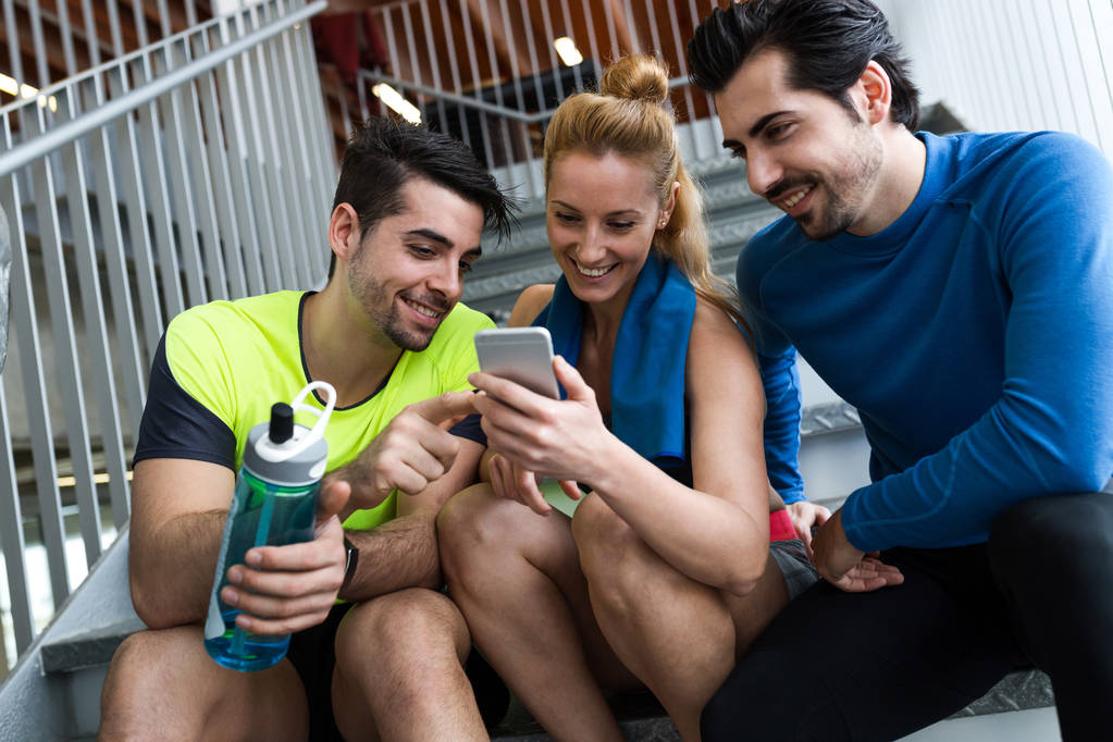 Ομάδα των σπορ των ανθρώπων που χρησιμοποιούν κινητό τηλέφωνο στο γυμναστήριο. - Φωτογραφία, εικόνα