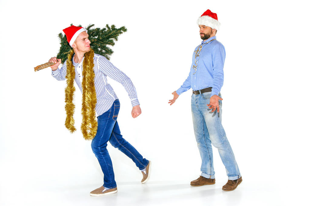 der junge Mann mit der Weihnachtsmütze, der den Weihnachtsbaum trägt - Foto, Bild