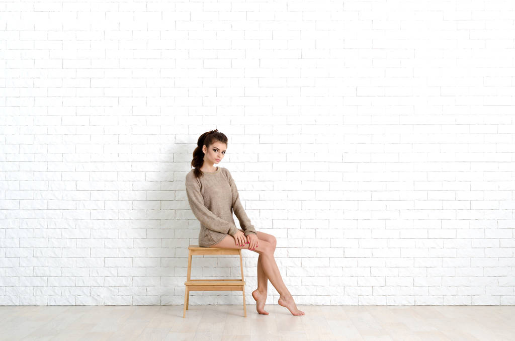 Молода і красива жінка сидить на дерев'яному стільці. Вона носить в'язаний светр. Фото дуже ніжне і затишне
. - Фото, зображення