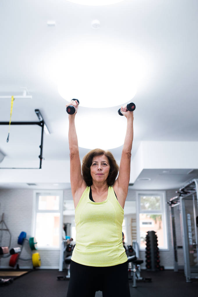 Mujer mayor en el gimnasio haciendo ejercicio con pesas
. - Foto, imagen