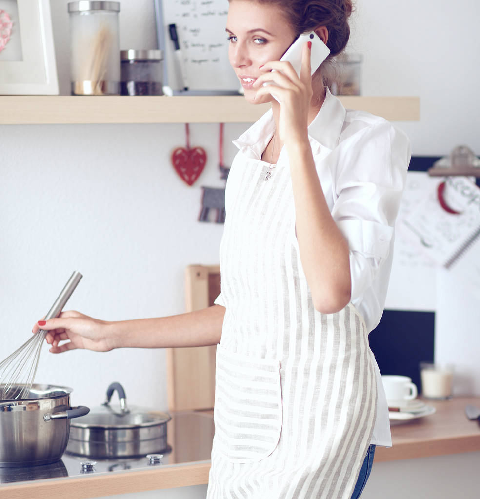Портрет усміхнена жінка з телефоном на кухні вдома
 - Фото, зображення