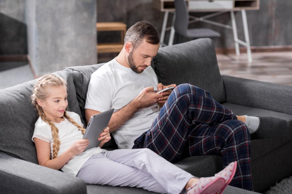 Padre e hija usando dispositivos digitales
 - Foto, imagen