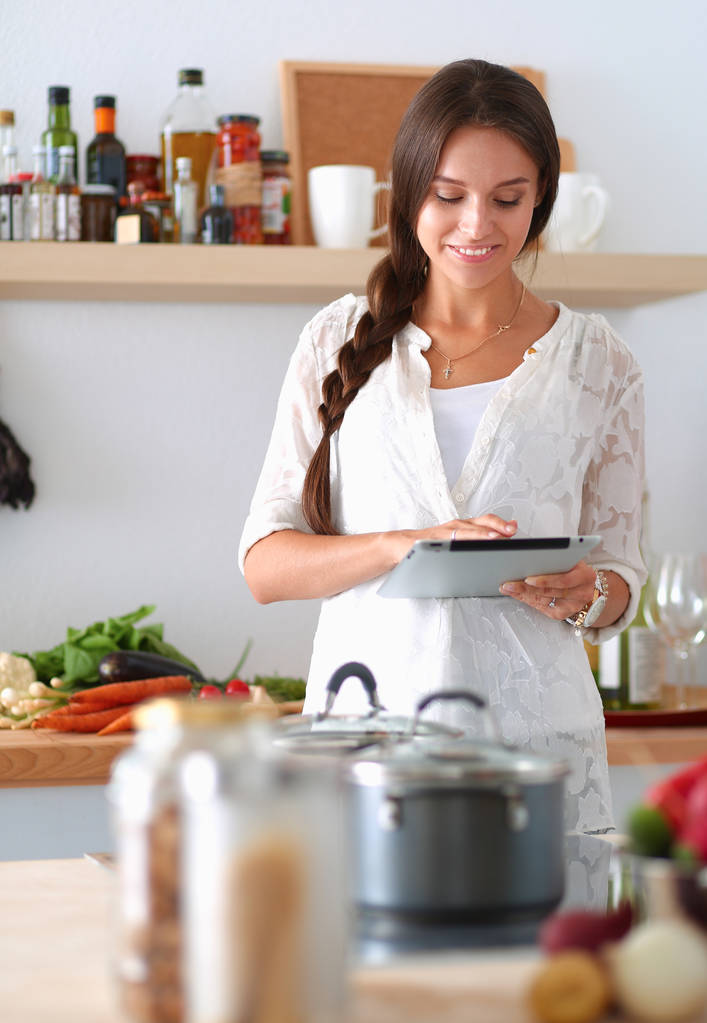 Jonge vrouw met behulp van een tablet computer om te koken in haar keuken - Foto, afbeelding