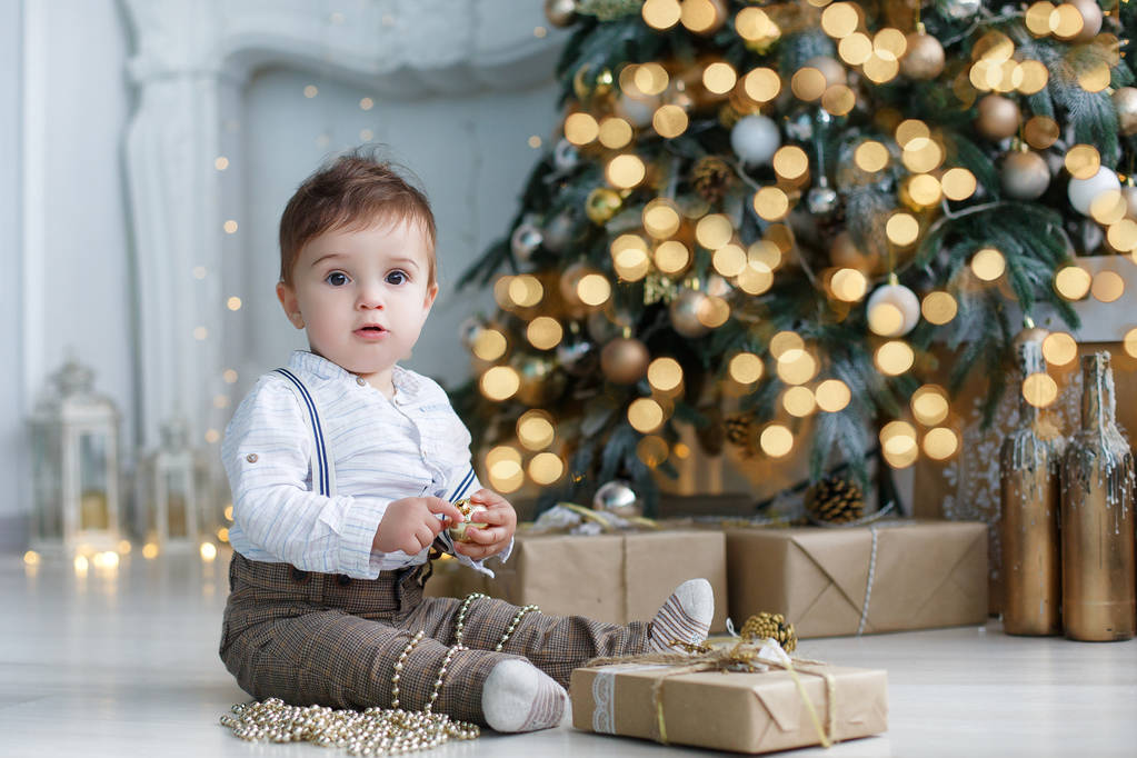 Mooie babe zit in de buurt van de kerstboom en geschenkverpakkingen - Foto, afbeelding