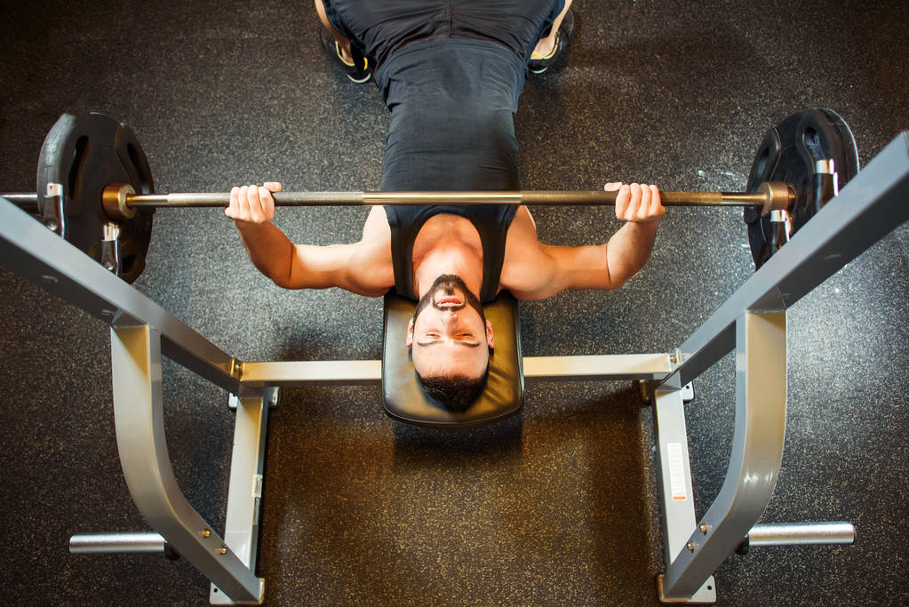 Mladý muž v tělocvičně cvičení hrudníku na Bench pressu - Fotografie, Obrázek