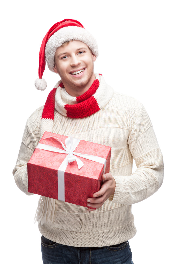 Молодой человек в шляпе Санты держит большой красный рождественский подарок
 - Фото, изображение