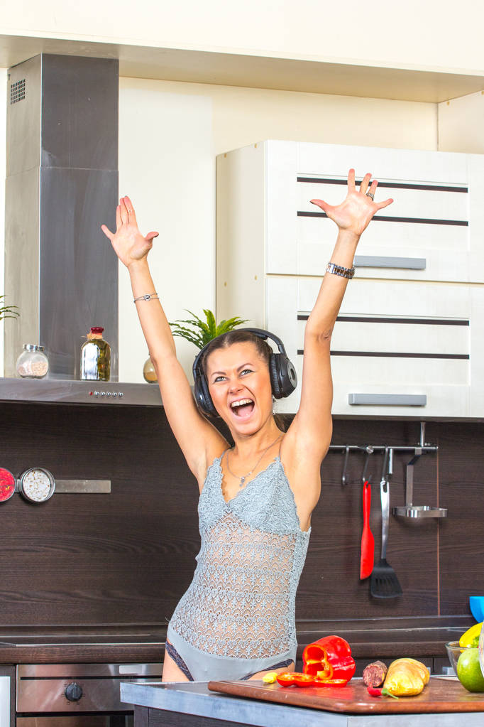 fröhliche junge Frau tanzt in Küche mit Kopfhörern.  - Foto, Bild