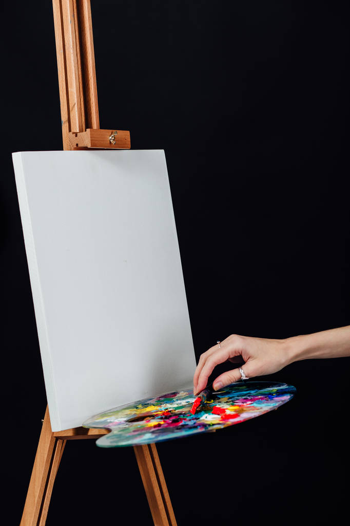 Roztomilá krásná dívka umělec maluje obraz na plátně stojan. Prostor pro text. Studio černé pozadí. - Fotografie, Obrázek