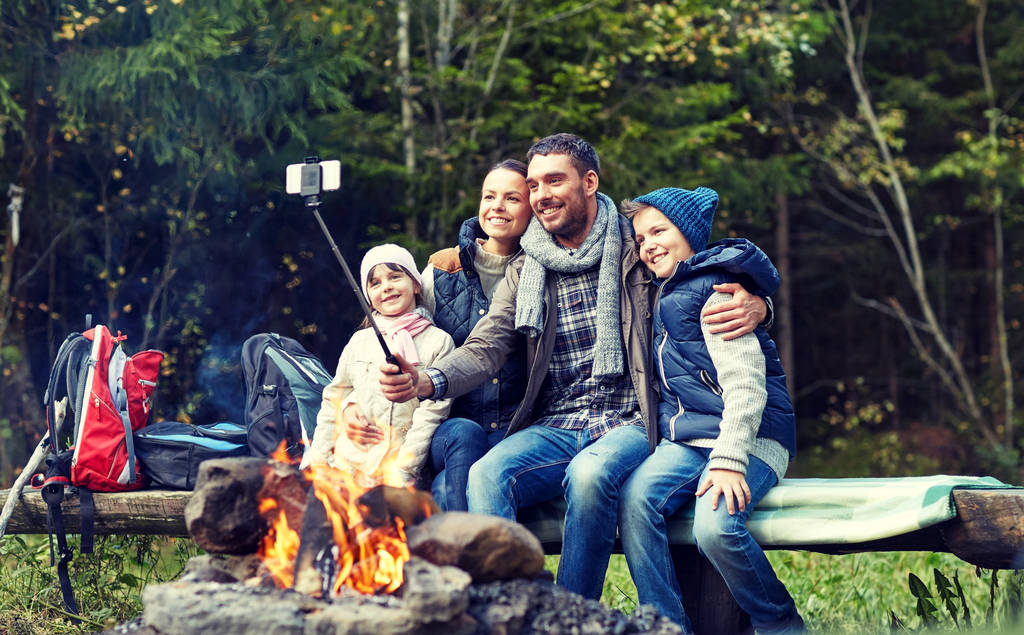 familia con smartphone tomando selfie cerca de fogata
 - Foto, Imagen