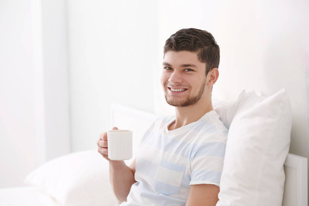 Красивый молодой человек пьет кофе дома - Фото, изображение